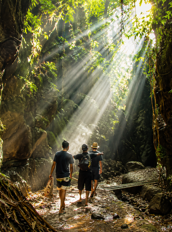 Travelers exploring the stunning Beji Guwang Hidden Canyon in Bali, featuring dramatic rock formations, crystal-clear river water, and lush tropical scenery.